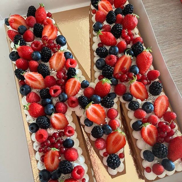 Letter Cake avec la lettre M, une chantilly à la vanille et des fruits rouges joliement parsemés sur le dessus. Fraises, mures, myrtilles et groseilles.